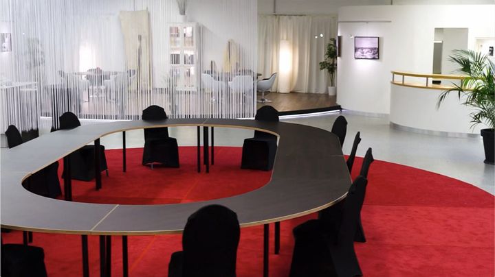 Moderner Konferenztisch mit runder Sitzgruppe auf rotem Teppich in hellem Raum.