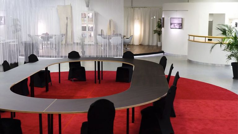 Moderner Konferenztisch mit runder Sitzgruppe auf rotem Teppich in hellem Raum.